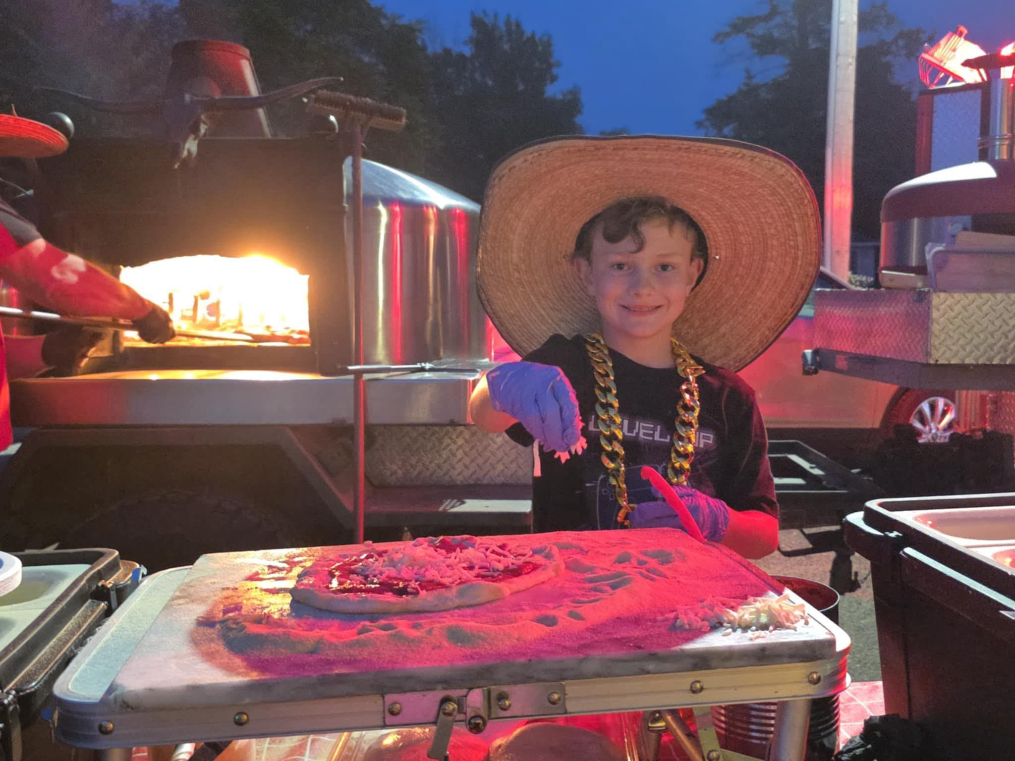 Kid making pizza at the wood-fired oven